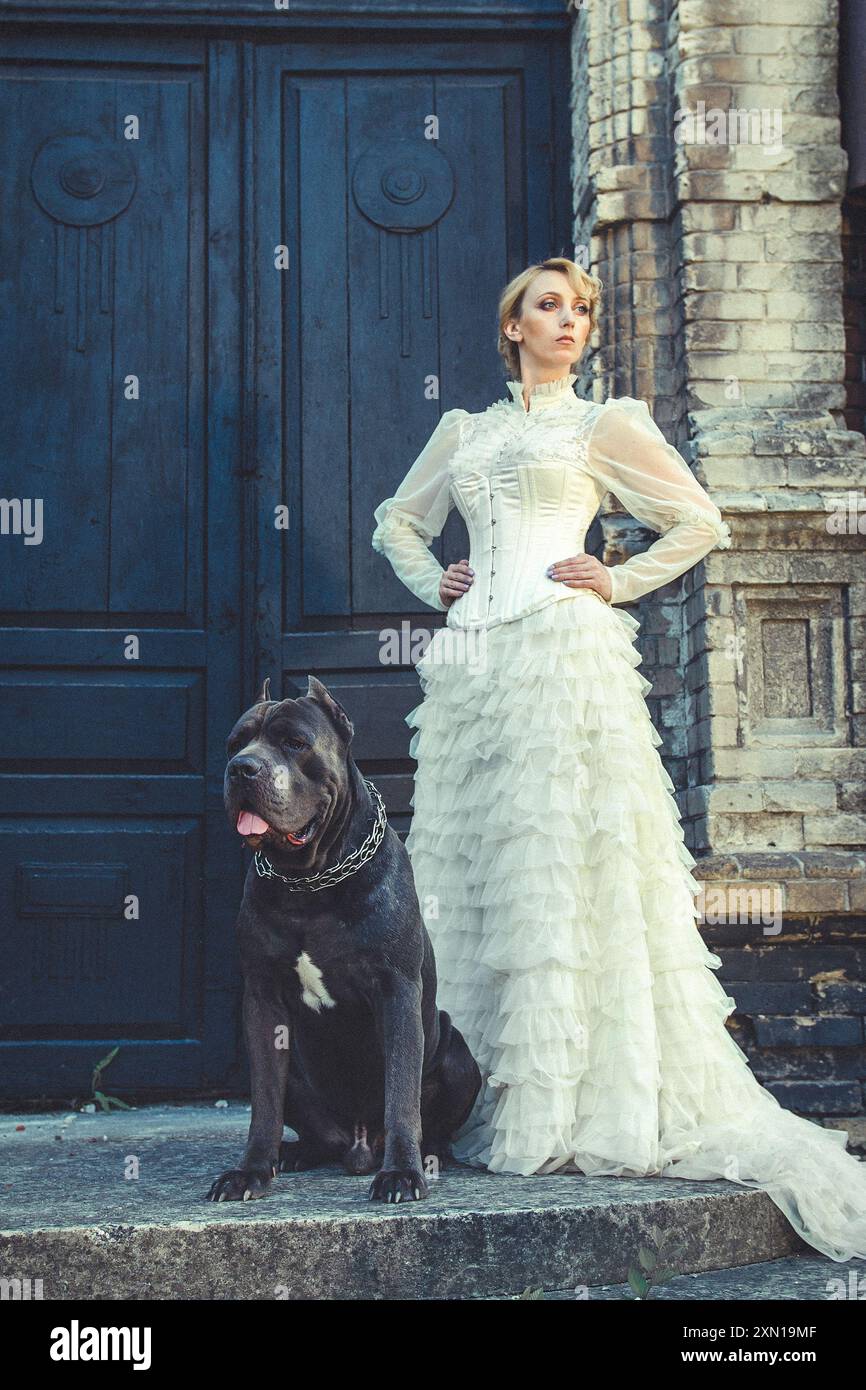 Mädchen in einem alten Kleid mit Rüschen und einem großen dunklen Hund Stockfoto