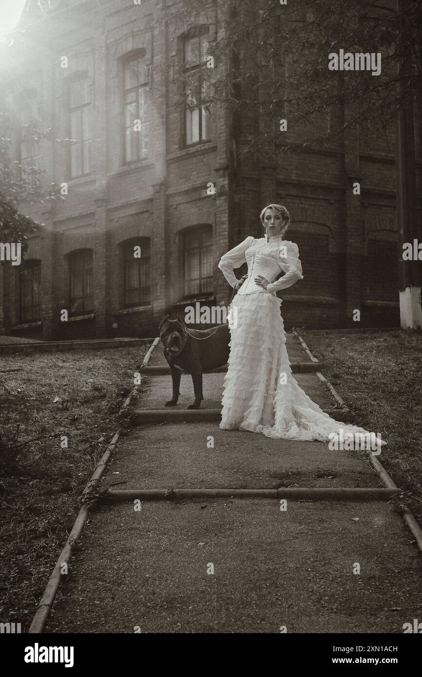 Mädchen in einem alten Kleid mit Rüschen und einem großen dunklen Hund Stockfoto