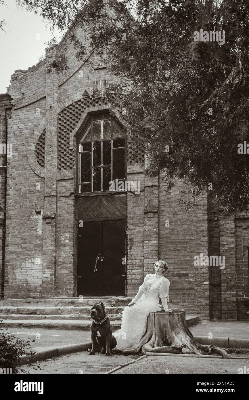 Mädchen in einem alten Kleid mit Rüschen und einem großen dunklen Hund Stockfoto