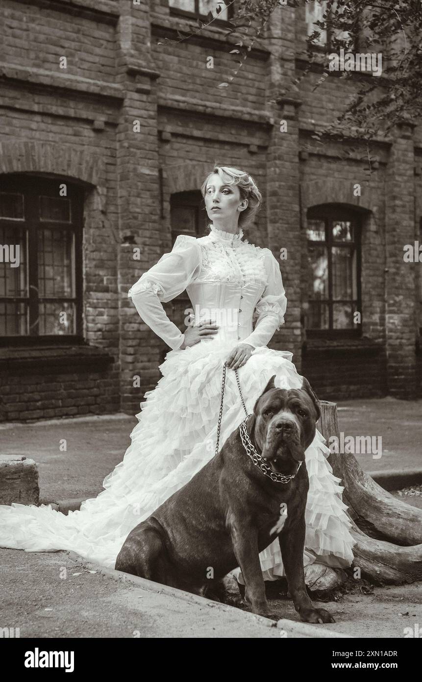 Mädchen in einem alten Kleid mit Rüschen und einem großen dunklen Hund Stockfoto