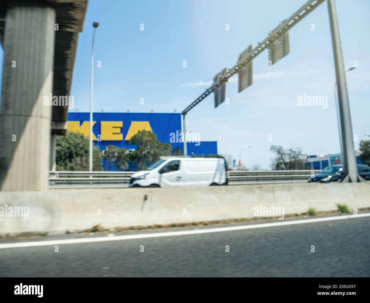 Palma, Spanien - 28. Juni 2023: Unscharfer Blick auf eine Straßenszene mit einer Brücke, einem Van und einem IKEA-Geschäft im Hintergrund, was die verschwommene Bewegung und Fernsicht des Gewerbebetriebs unterstreicht Stockfoto