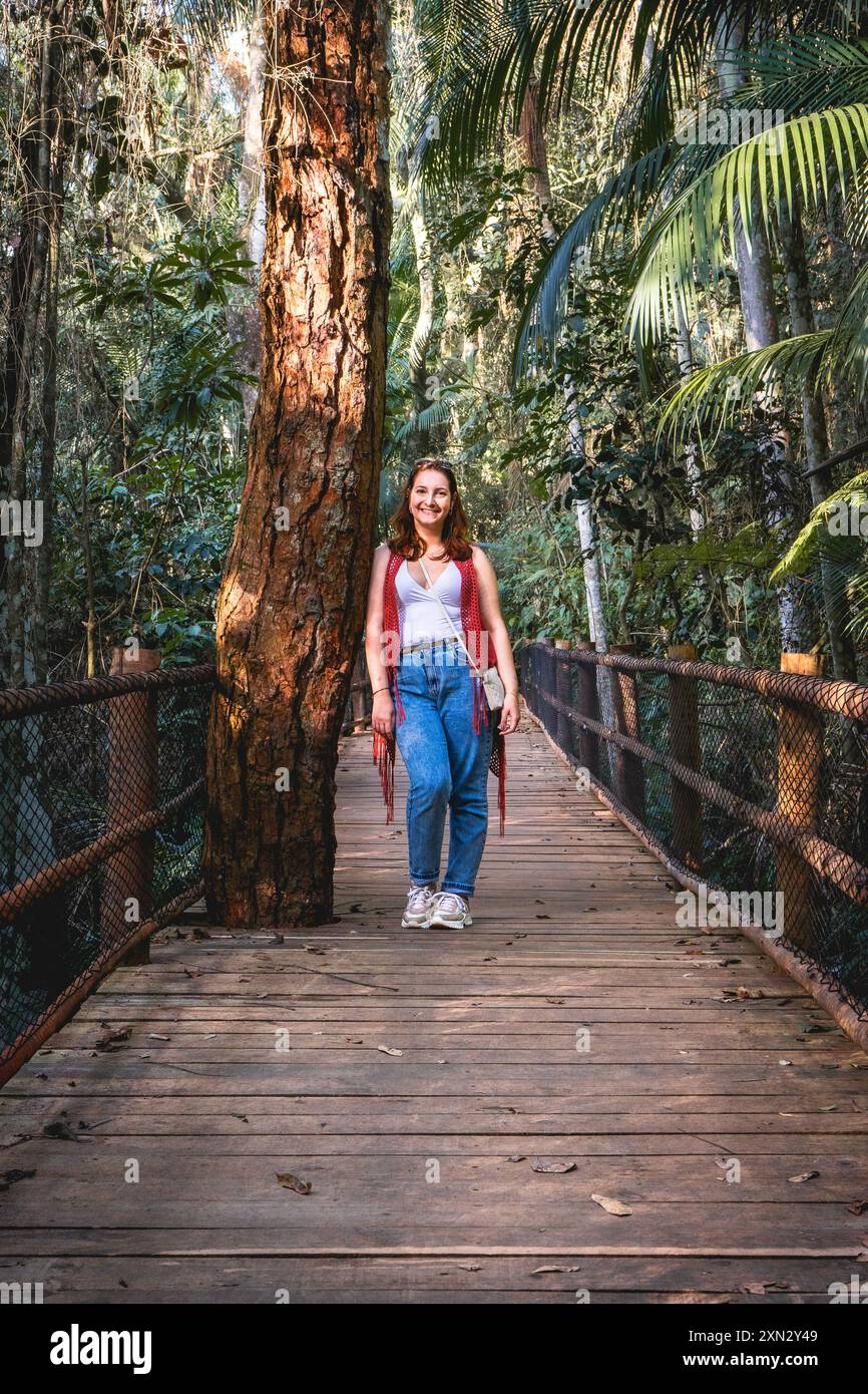 Brasilianische Frau mit rotem Pullover, stehend auf einer Holzbrücke an einem Wanderweg. Jardim Botanic Garden, São Paulo, Brasilien. Stockfoto