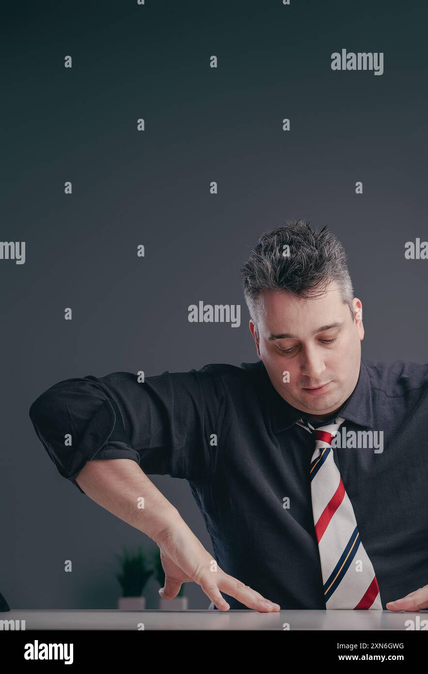 Ein reifer Geschäftsmann im Alter von 40 Jahren lehnt sich nachdenklich auf einen eleganten Schreibtisch in einem modernen Büro und strahlt Professionalität und Konzentration aus Stockfoto