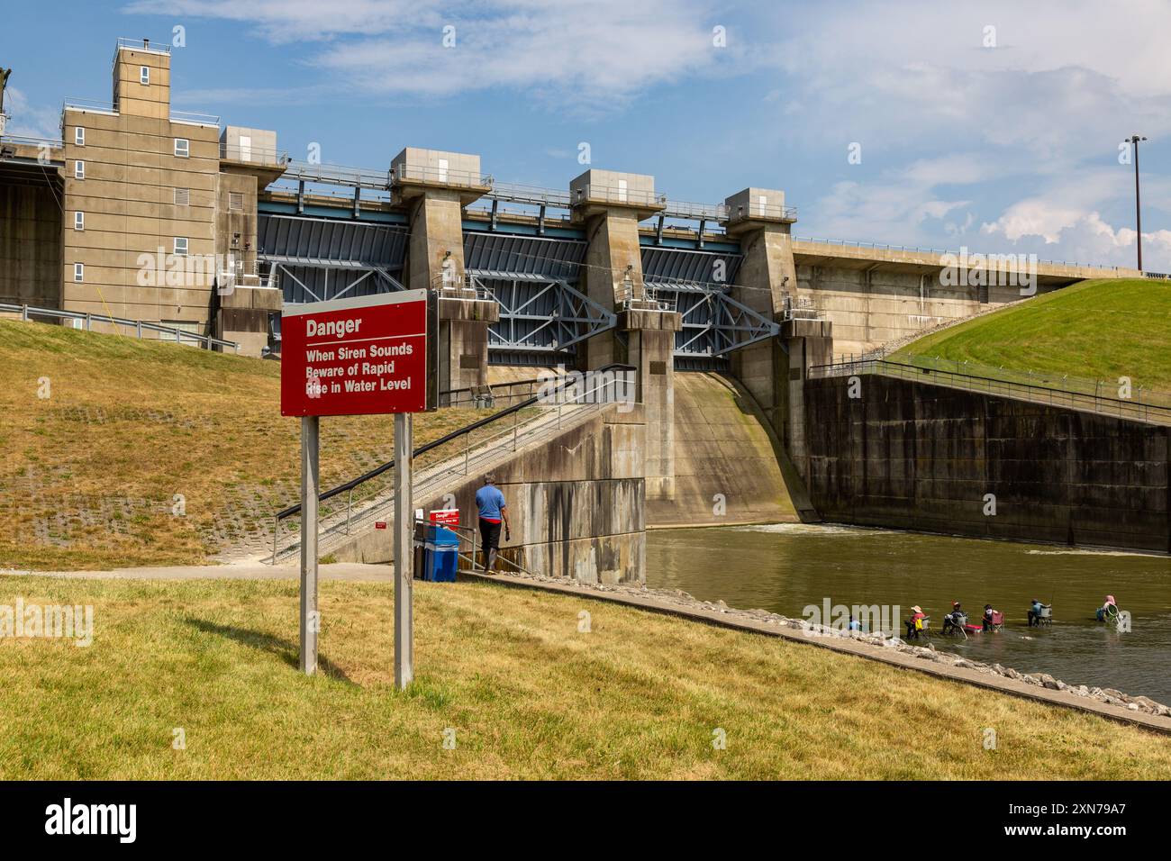 Am J. Edward Roush Dam in der Nähe von Huntington, Indiana, USA, sitzen Fischer unterhalb des Überflusses, direkt hinter einem Schild, das sie vor einem möglichen aufsteigenden Wasser warnt. Stockfoto Am J. Edward Roush Dam in der Nähe von Huntington, Indiana, USA, sitzen Fischer unterhalb des Überflusses, direkt hinter einem Schild, das sie vor einem möglichen aufsteigenden Wasser warnt. Stockfoto
