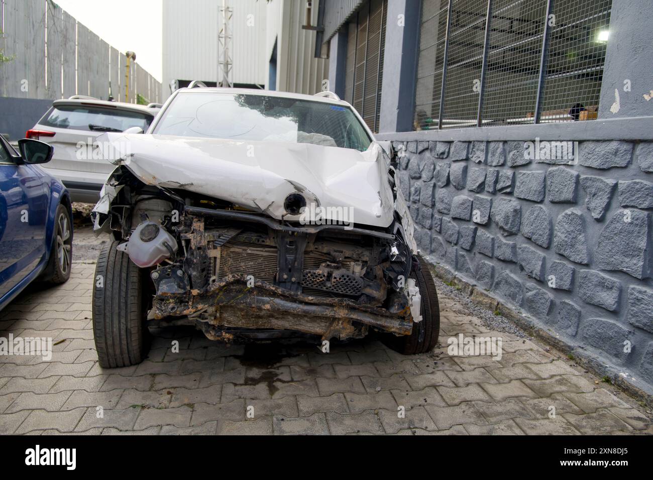 Ein weißes Auto, das bei einer Kollision schwer beschädigt wurde, sitzt auf einer Straße der Stadt, eine deutliche Erinnerung an die Auswirkungen von Unfällen. Stockfoto
