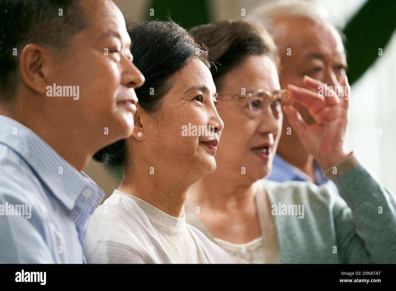 Seitenansicht einer Gruppe älterer asiatischer Leute, zwei Paare, die zu Hause auf der Couch sitzen und fernsehen Stockfoto