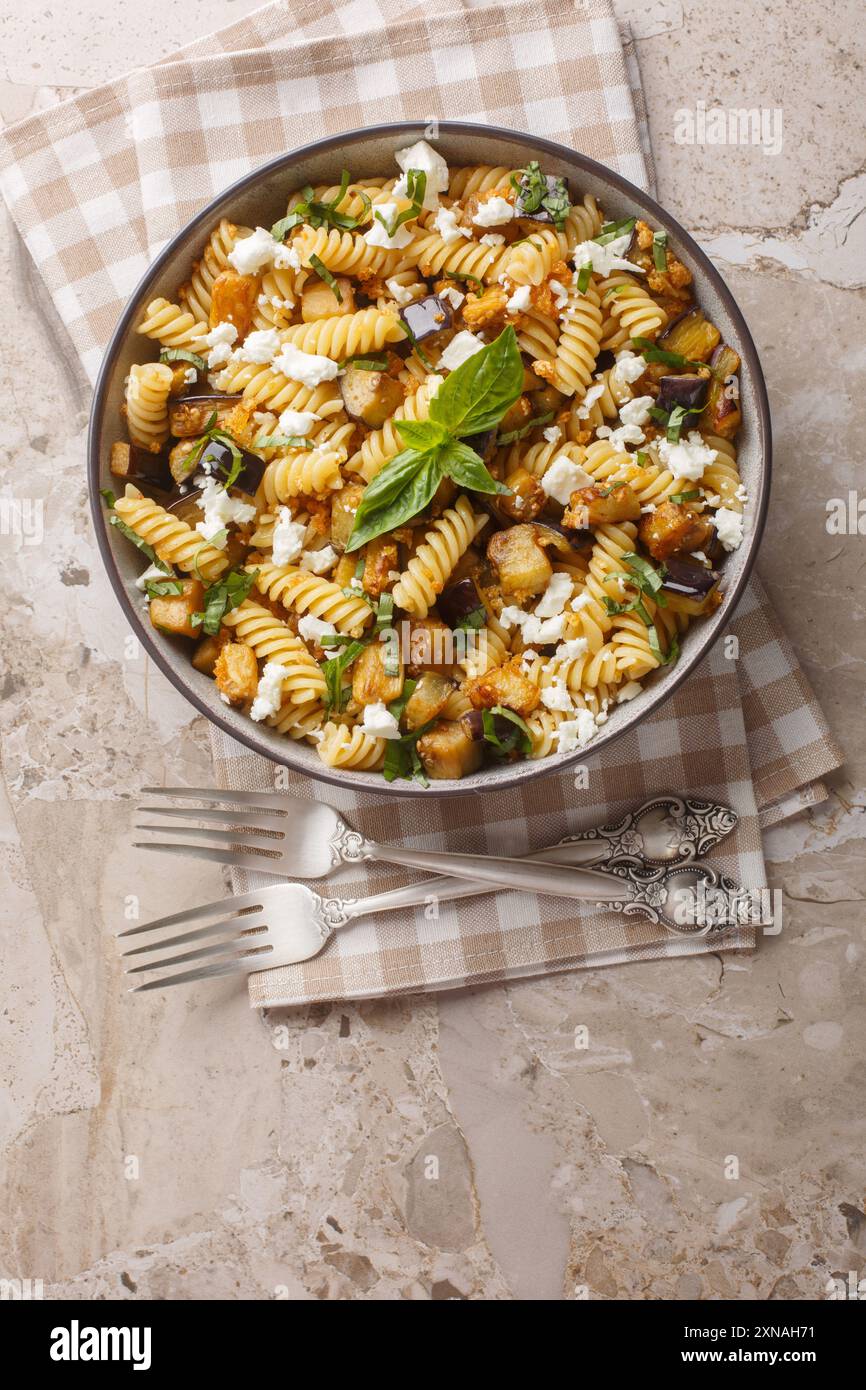 Fusilli-Pasta mit gebratener Aubergine, Knoblauch und Fetakäse in einer Schüssel auf dem Tisch. Vertikale Draufsicht von oben Stockfoto