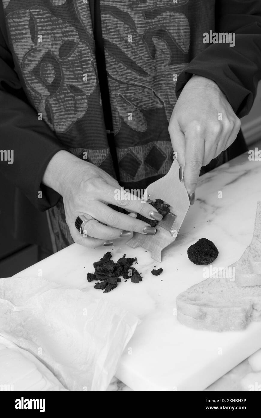 Nahaufnahme von weiblichen kaukasischen Händen, die schwarze Diamanttrüffel schneiden, um ein Gourmet-Sandwich mit Sauerteigbrot zuzubereiten. USA Stockfoto
