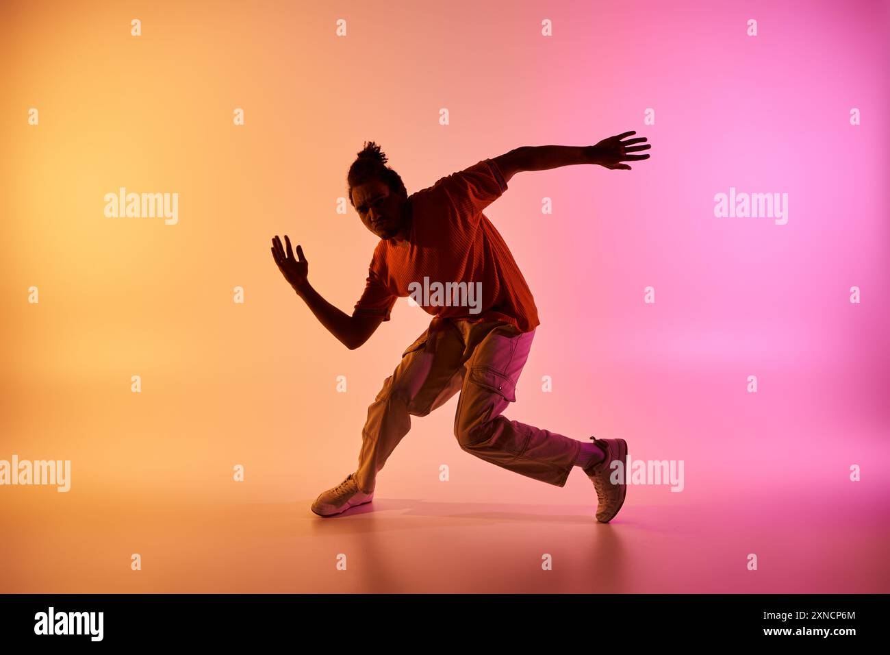 Ein junger afroamerikanischer Tänzer spielt in einem Studio einen Hip-Hop-Tanz vor einem farbenfrohen Hintergrund. Stockfoto