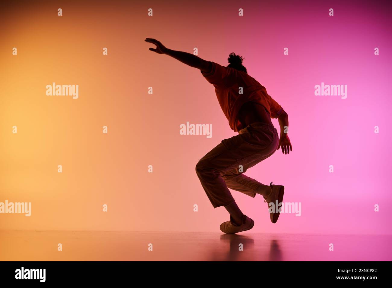 Ein junger Afroamerikaner tanzt vor einem lebendigen Hintergrund. Er wird in der Luft gefangen und zeigt seine dynamischen Bewegungen. Stockfoto