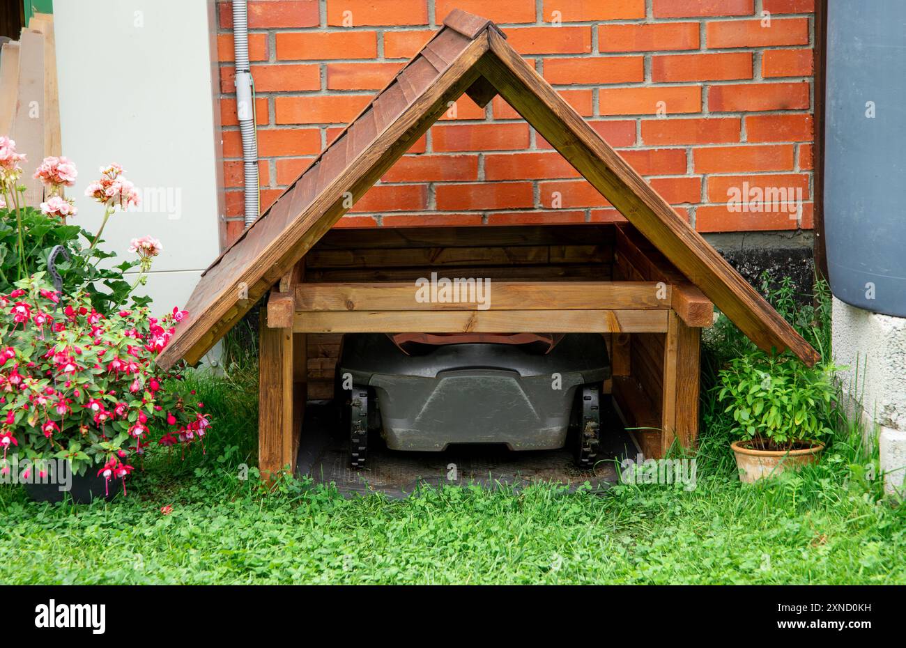 Roboter-Rasenmäher in hausgemachter Holz-Rasenmäher-Garage im Freien im Sommer im Garten zu Hause. Stockfoto