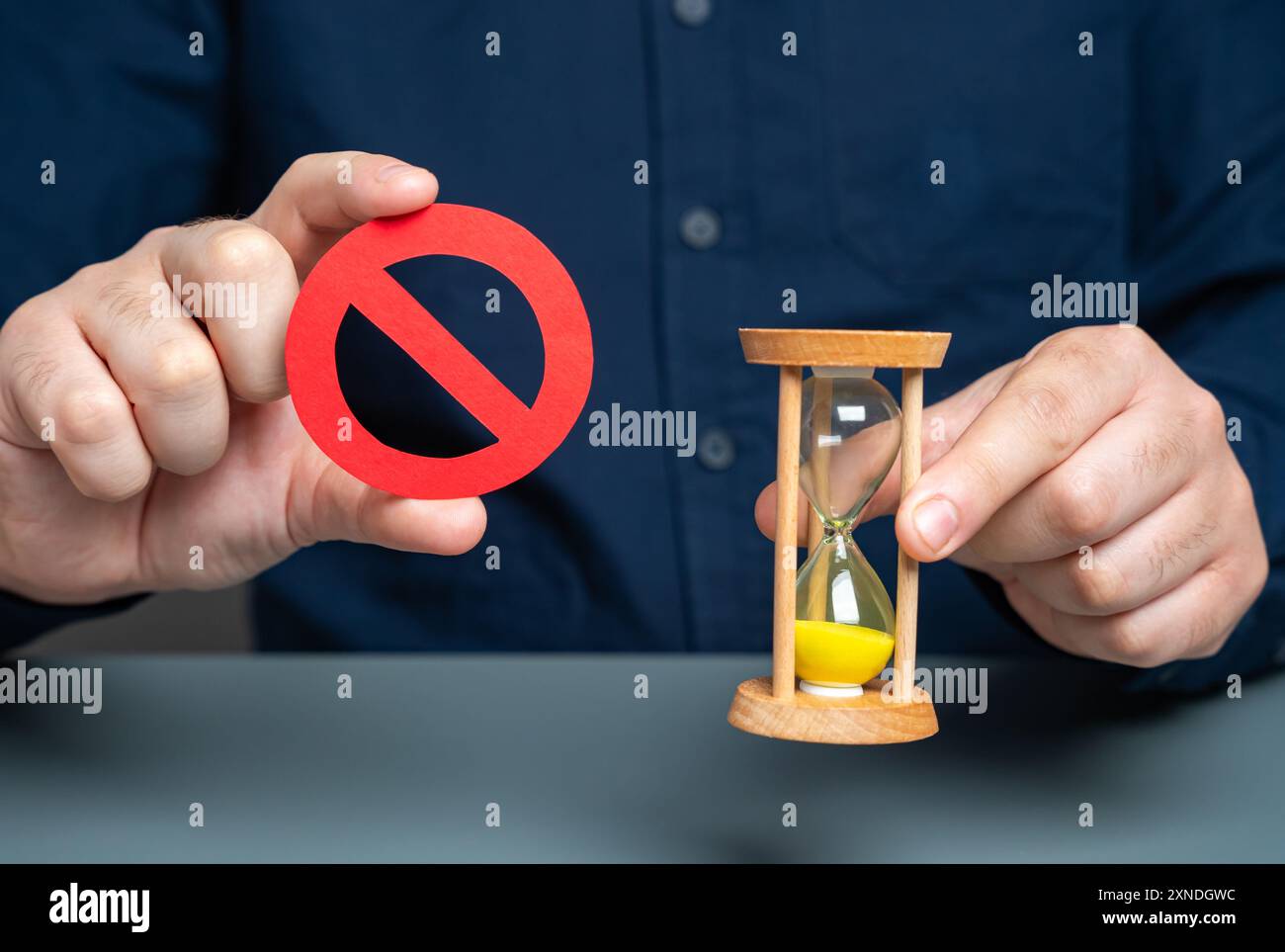 Ein Mann hält ein rotes NO-Zeichen und eine Sanduhr. Die Zeit läuft ab. Terminannahmen. Ein wichtiges Verbot muss unverzüglich eingehalten werden. Temporar Stockfoto