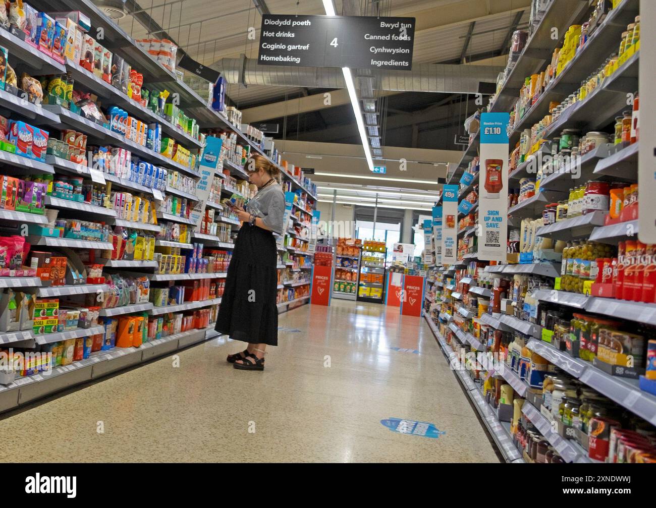 Junge Frau Teenager, die Zutaten und Preis von Tee im Supermarktgang untersucht und auf Verpackungen, Dosen in Regalen sieht UK Juli 2024 KATHY DEWITT Stockfoto