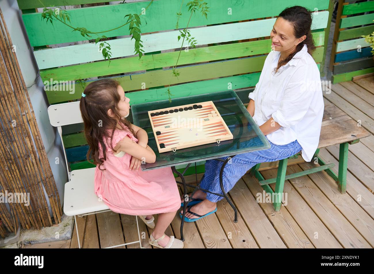 Mutter und Tochter spielen gemeinsam im Freien Backgammon. Familienbeziehungen, schöne Zeit und Freizeitaktivitäten. Glückliche Momente und Entspannung in einem Casu Stockfoto