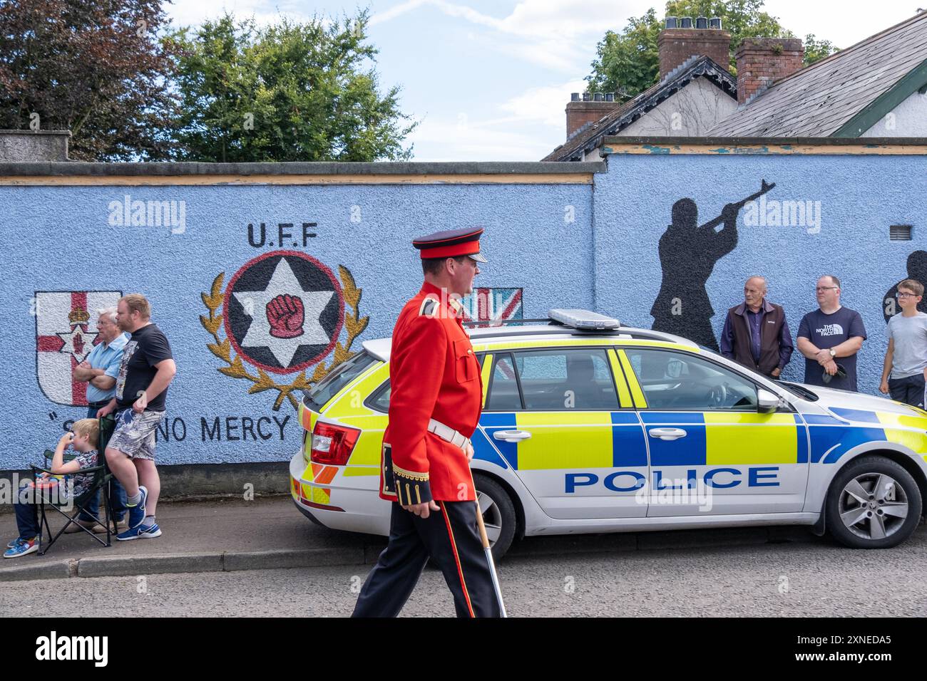 Ballyclare, Nordirland - 27. August 2022: Bandsman passiert UFF Paramilitary Wandgemälde und PSNI Police Car, letzten Samstag Royal Black Institution. Stockfoto