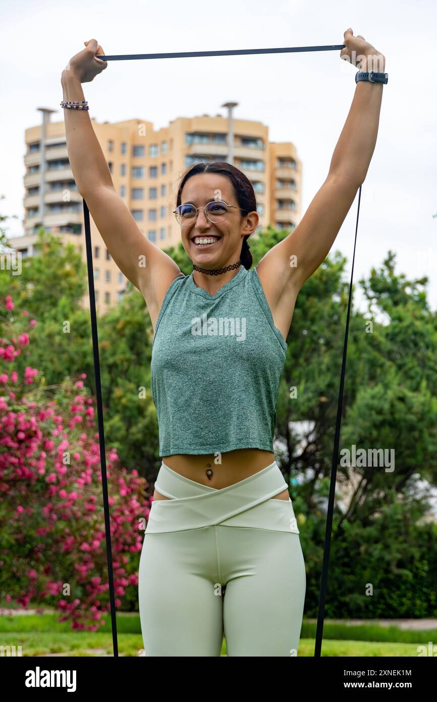 Eine junge Frau trainiert in einem Park mit einem Widerstandsband, genießt ihre Fitness-Routine und konzentriert sich auf das Wohlbefinden in einer friedlichen Umgebung im Freien Stockfoto