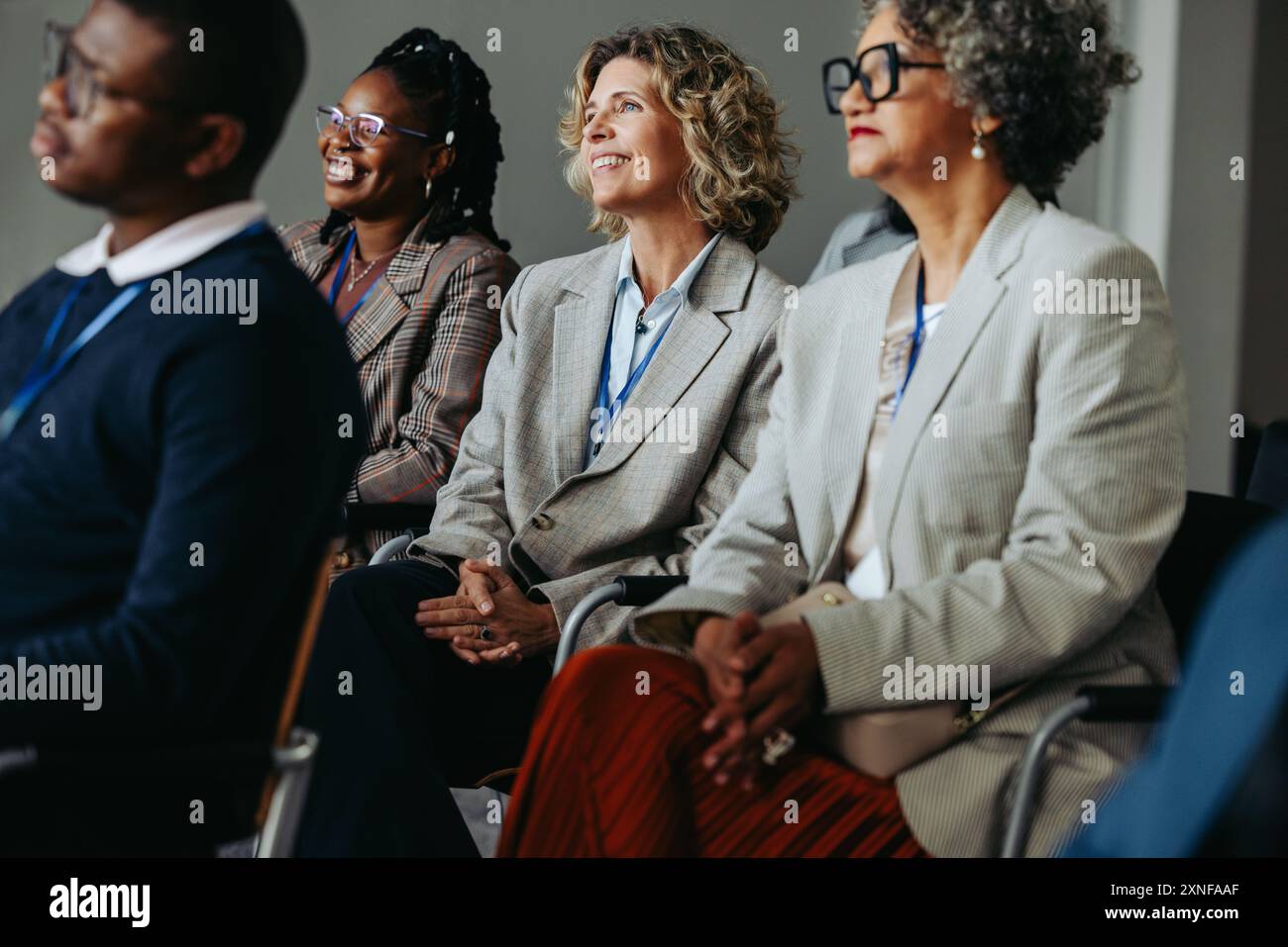 Reife Geschäftsfrauen und Kollegen, die an einer Workshop-Präsentation teilnahmen, in einem Konferenzpublikum sitzen, aufmerksam zuhören und lächeln. Stockfoto