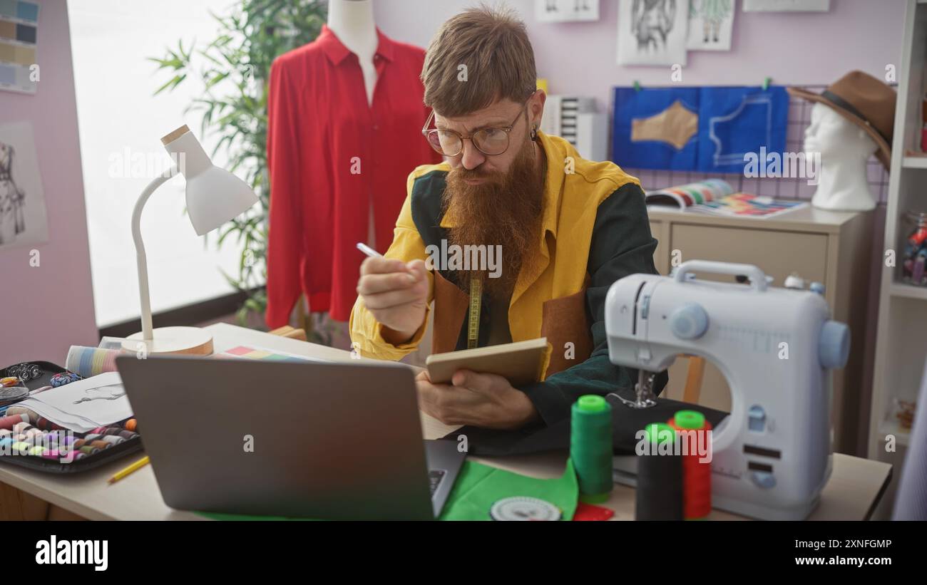Rothaariger Mann mit Bart macht Notizen in einem Schneiderladen, umgeben von Nähartikeln, Puppen und Kleidungsstücken. Stockfoto