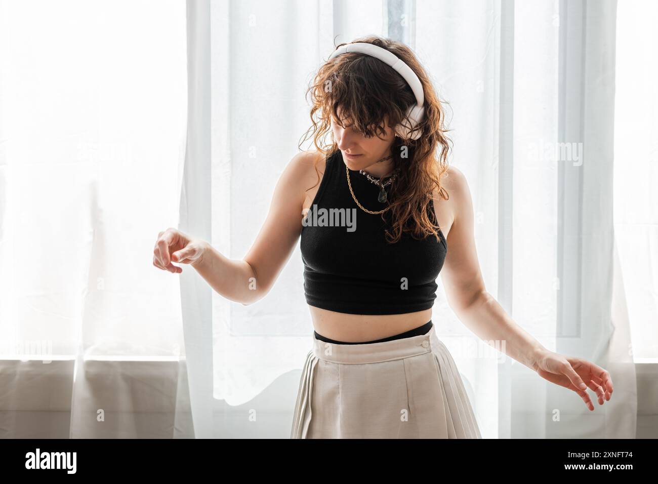 Die Frau tanzt vor dem Fenster, während sie Musik auf ihren Kopfhörern hört. Stockfoto