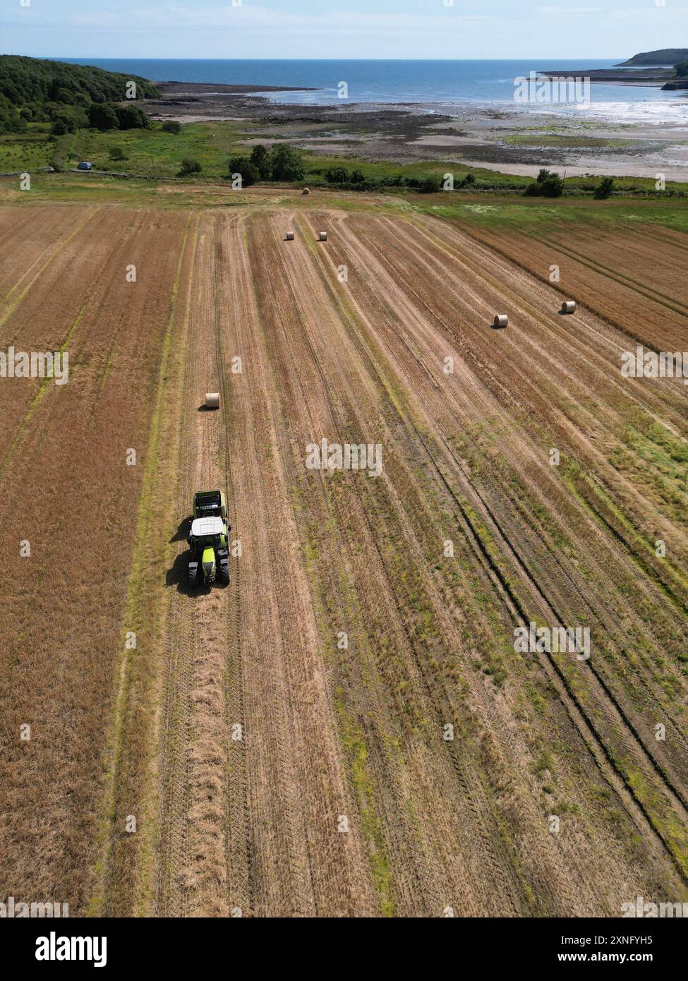 Garlieston, Wigtownshire, Schottland, Großbritannien - Mittwoch, 31. Juli 2024 – Luftaufnahme von Landwirten, die an einem sonnigen warmen Tag Weizenstängel für die Strohernte in den Feldern der ländlichen Küstenregion Dumfries & Galloway ballen – die lokalen Temperaturen erreichten 22c mit Regenvorhersage für Freitag – Foto Steven May / Alamy Live News Stockfoto