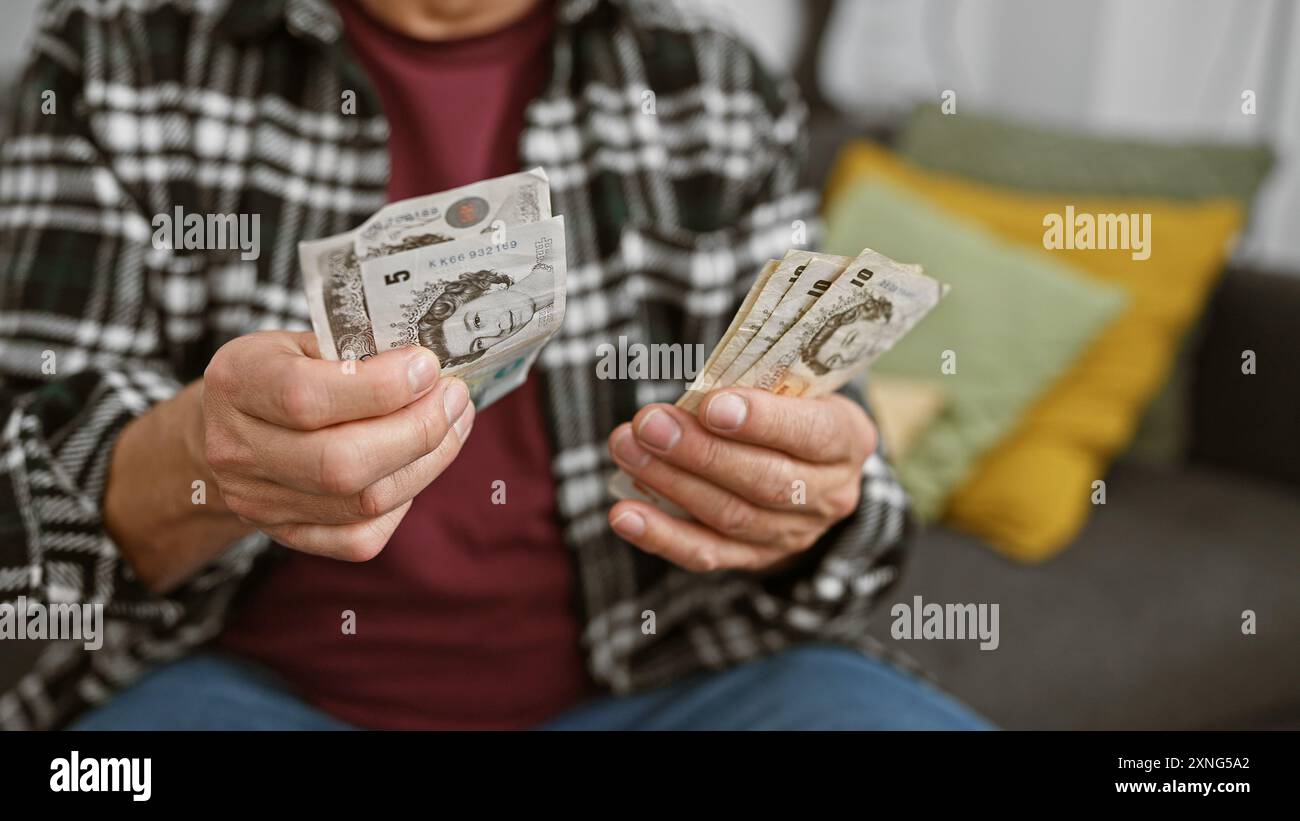 Ein reifer Mann zu Hause, der britische Pfund hält, was Finanzplanung oder Budgetierung in einem komfortablen Wohnzimmer bedeutet. Stockfoto
