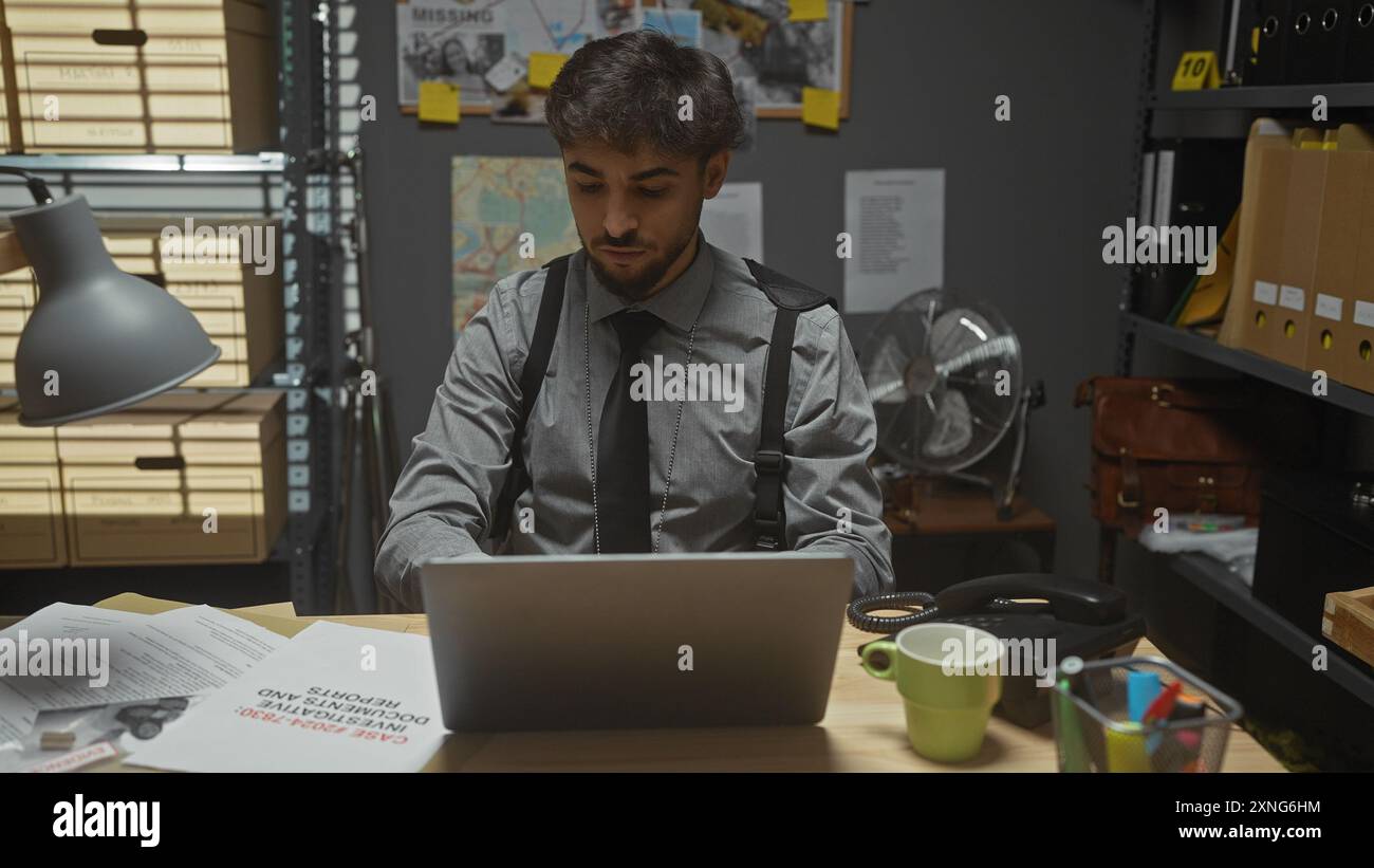 Schöner arabischer Mann mit Bart, der an einem Laptop in einem Detektivbüro arbeitet, umgeben von Akten und einer Tafel mit Fotos. Stockfoto