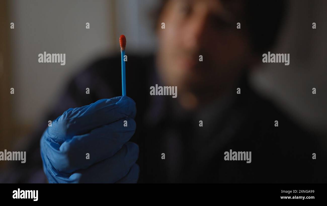 Ein fokussierter Mann untersucht Beweise mit einem Q-Tipp an einem Tatort drinnen, um Ermittlungen und Analysen zu übermitteln. Stockfoto