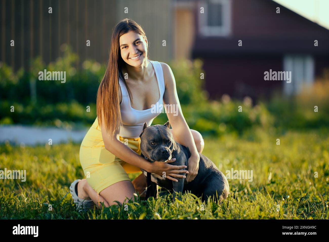 Außenporträt einer jungen weißen Frau mit einem amerikanischen Bullie, der ihre Zunge ausstreckt, einer europäischen Frau, die ihren Hund vor dem Hintergrund des ländlichen L kuschelt Stockfoto