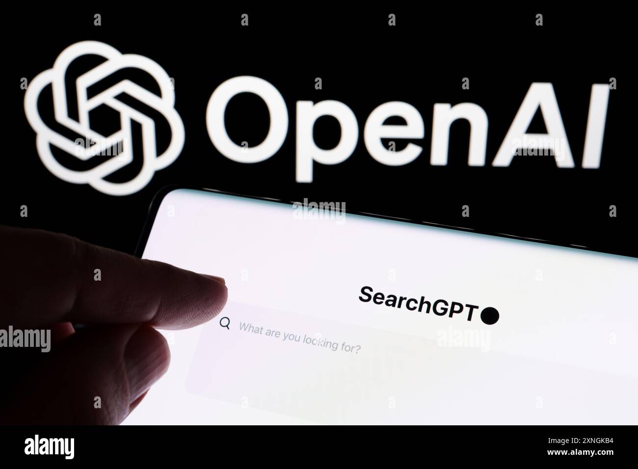 Die Hand zeigt auf die SearchGPT-Seite, die auf dem Smartphone zu sehen ist, und das offizielle OpenAI-Firmenlogo im Hintergrund. Neues AI-Suchwerkzeug. Stafford, Vereinigtes Königreich, J Stockfoto