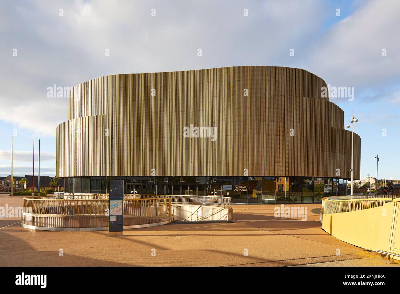 Landschaftlich gestaltetes öffentliches Gebiet und kurvenreiche Arena außen. Swansea Arena und Copr Bay Bridge, Swansea, Vereinigtes Königreich. Architekt: acme, 2024. Stockfoto