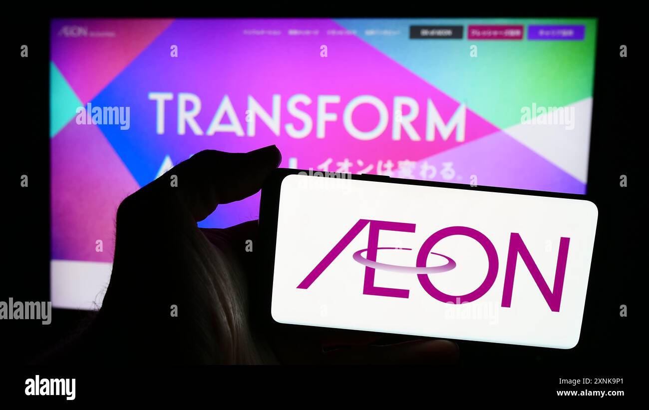 Person mit Smartphone und Logo der japanischen Einzelhandelsgesellschaft Aeon Co. Ltd. Vor der Website. Schwerpunkt auf dem Display des Telefons. Stockfoto