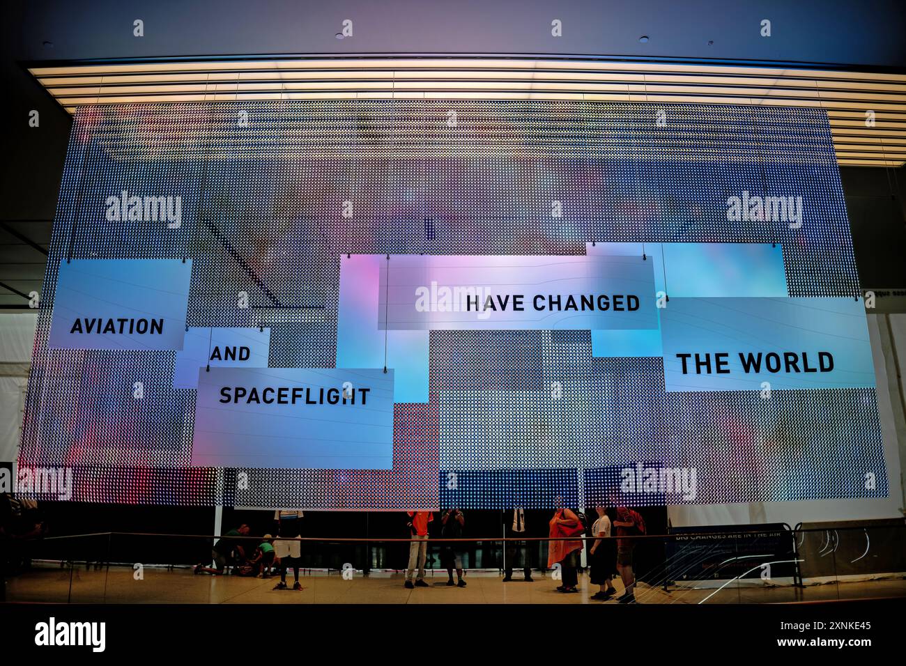Smithsonian National Air and Space Museum Foyer Display Washington DC | WASHINGTON D.C., Vereinigte Staaten – Besucher halten unter einer aufgehängten LED-Anzeige mit der Aufschrift „Luftfahrt und Raumfahrt haben die Welt verändert“ im Eingangsfoyer des National Air and Space Museum inne. Die Gitterbildinstallation stellt das zentrale Thema des Museums vor und rahmt die Galerien darüber hinaus als Aufzeichnung der Art und Weise ein, wie der Flug Reisen, Krieg, Wissenschaft und menschliche Ambitionen über wenig mehr als ein Jahrhundert hinweg veränderte. Stockfoto
