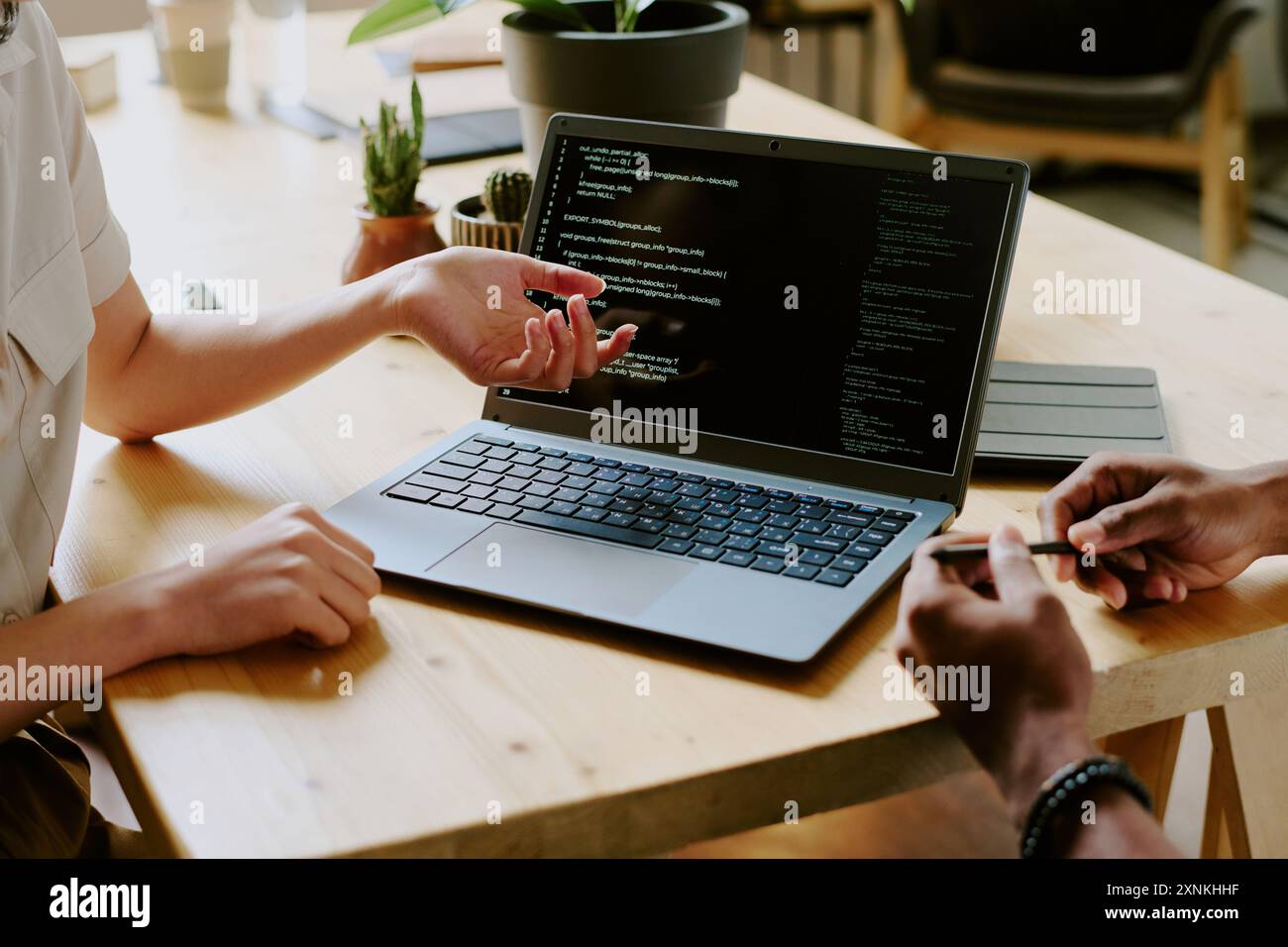 Nicht erkennbare birassische Programmierer, die am Holztisch sitzen und gemeinsam mit einem Laptop an Code arbeiten Stockfoto