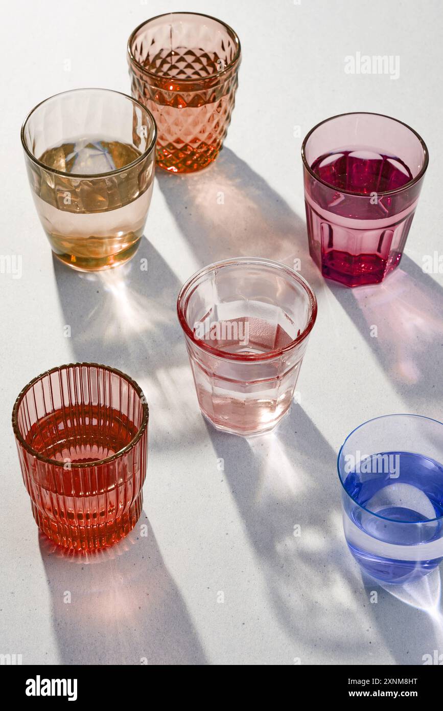 Verschiedene bunte Wassergläser auf grauem Hintergrund Stockfoto