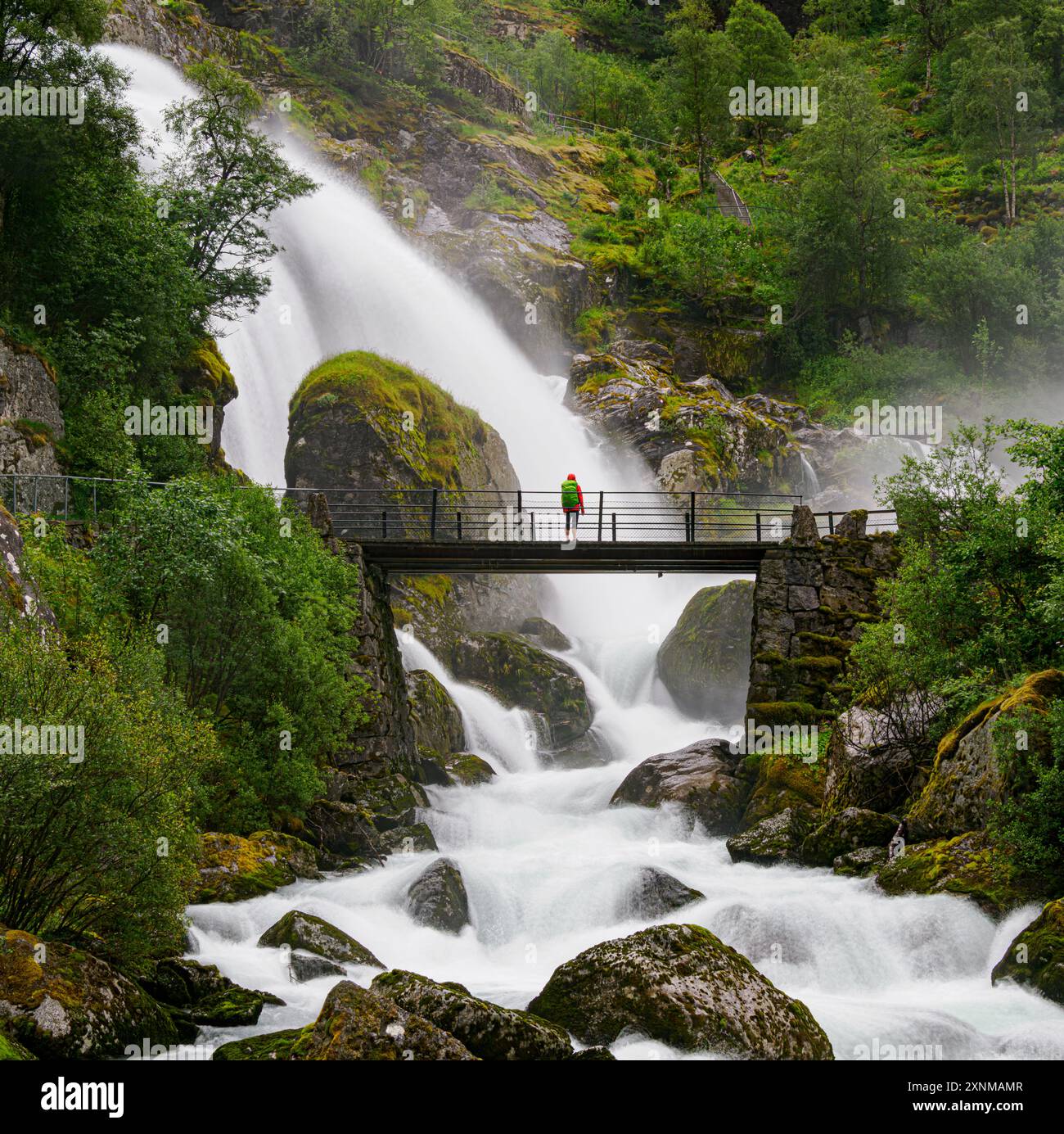 Walker auf der Brücke neben dem Kleivafossen-Wasserfall das Schmelzwasser des Jostedal-Gletschers stürzt eine steile Schlucht in Briksdal in Zentral-Norwegen ab Stockfoto