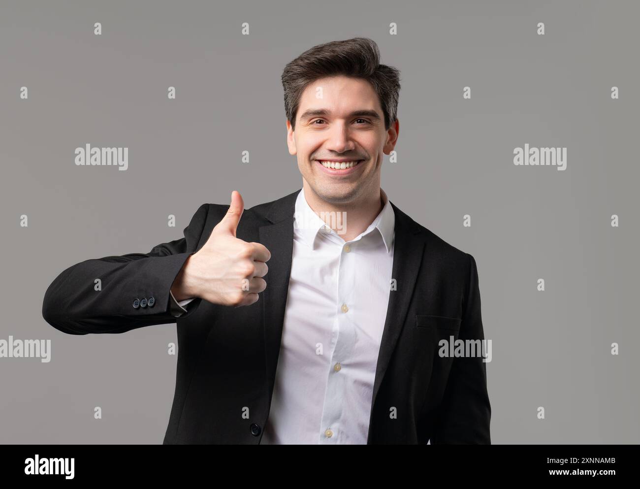 Geschäftsmann mit Handzeichen wie, Daumen hoch Geste. Glücklicher vorstandsvorsitzender auf Grau Stockfoto