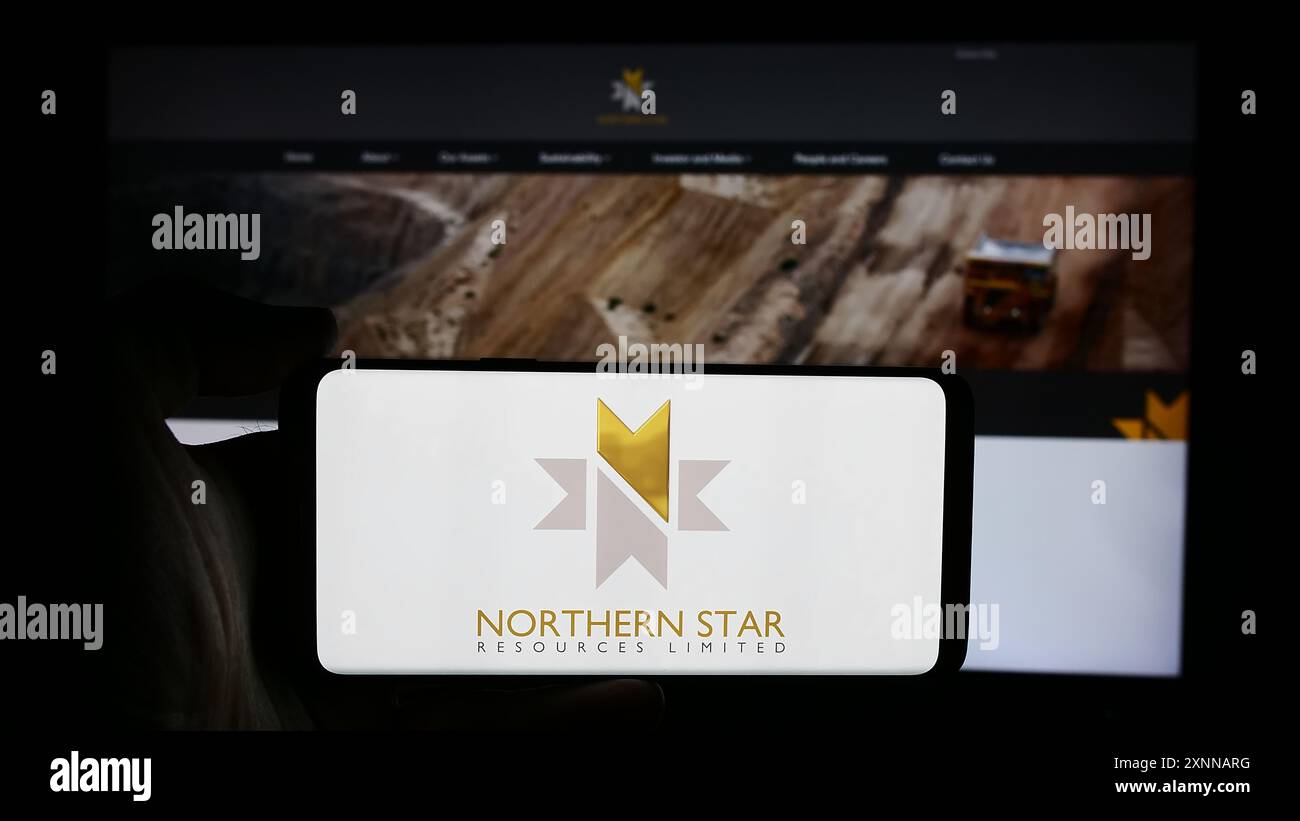 Person, die ein Mobiltelefon mit dem Logo der australischen Firma Northern Star Resources Limited vor der Webseite des Unternehmens hält. Schwerpunkt auf dem Display des Telefons. Stockfoto