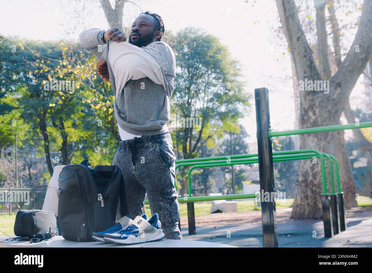 Junger afrikanischer Ethnicity-Mann draußen im Park, der einen Pullover auszieht, während er sich auf das Training vorbereitet, um sich auf die tägliche Trainingsroutine vorzubereiten. Stockfoto