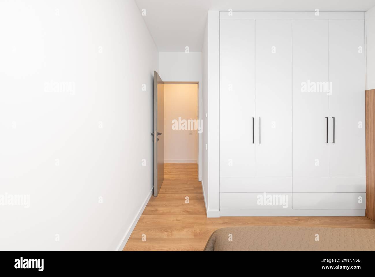 Luxuriöses Hauptschlafzimmer innen, modernes Haus, schöne Inneneinrichtung, Kingsize-Bett. Weißer Kleiderschrank, Schrank im Hintergrund. Öffnen Sie Die Holztür. Weitwinkel Stockfoto