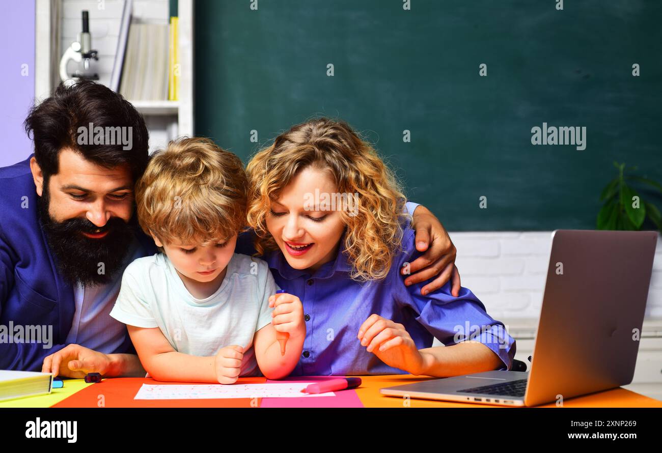 Erster Schultag. Kleiner Junge mit Vater und Mutter, die Hausaufgaben machen. Niedliches Kind, das Unterricht im Klassenzimmer studiert. Privatunterricht. Lehrer Mann und Frau h Stockfoto