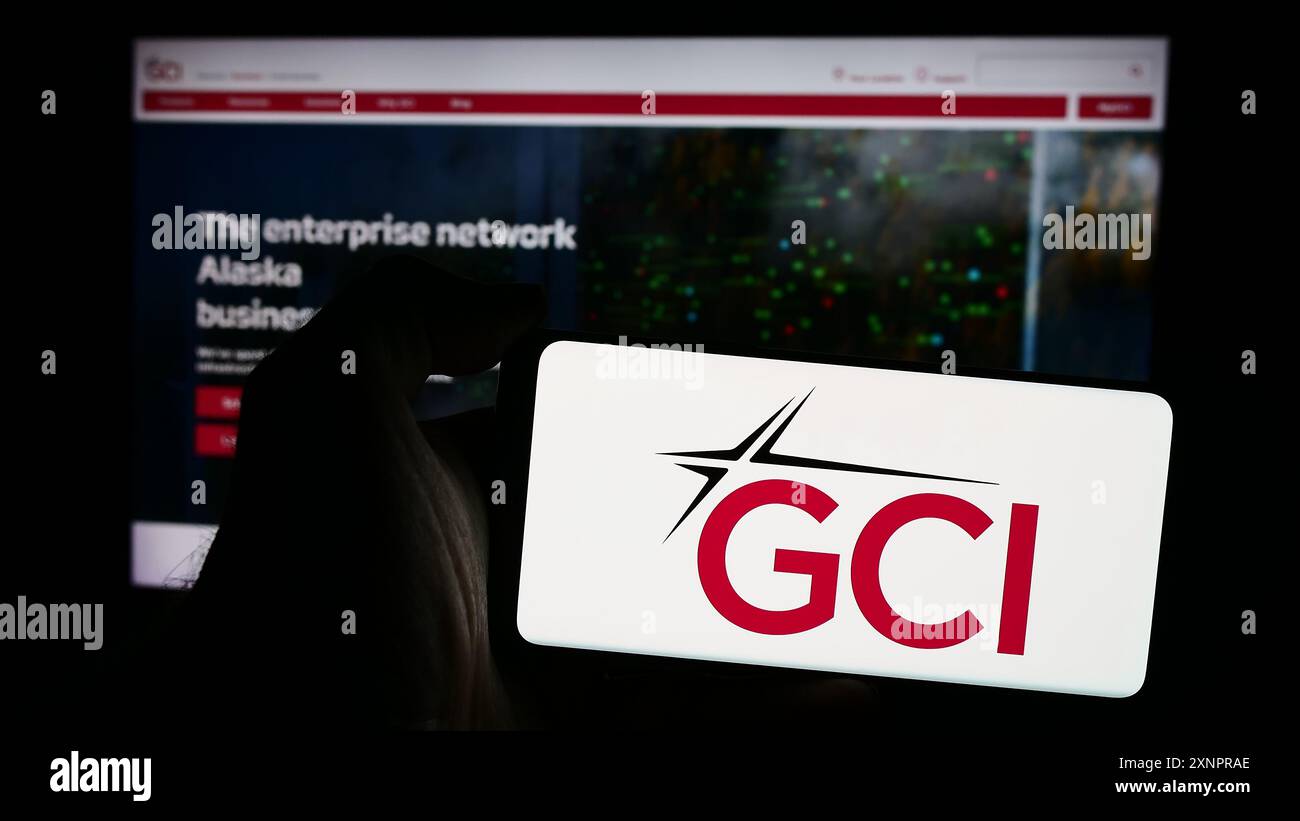 Person, die ein Mobiltelefon mit dem Logo des amerikanischen Telekommunikationsunternehmens GCI Communication Corp. Vor der Webseite hält. Schwerpunkt auf dem Display des Telefons. Stockfoto