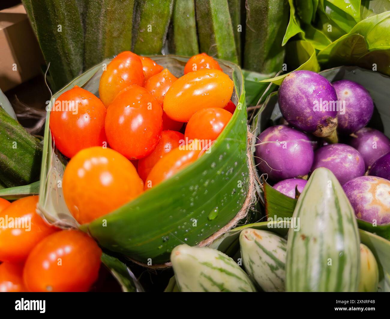 Nahaufnahme von frischen Tomaten/Paradeisern und verschiedenen Auberginen, einschließlich violetter und gestreifter Sorten, auf einem Markt in Bananenblättern ausgestellt. Stockfoto