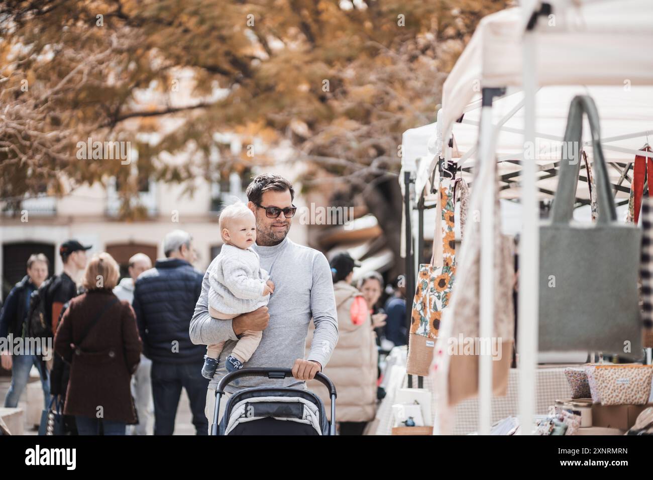 Vater geht mit seinem Kleinkind spazieren und schiebt einen Kinderwagen in einer Menschenmenge, die am Sonntag den Flohmarkt in Malaga, Spanien, besucht Stockfoto