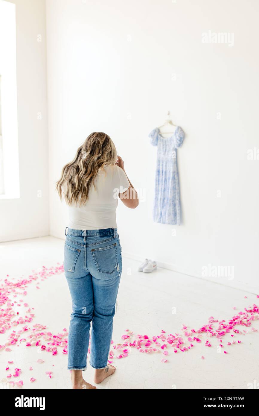 Frau, die inmitten rosafarbener Blüten steht und blaues Kleid an der Wand ansieht Stockfoto