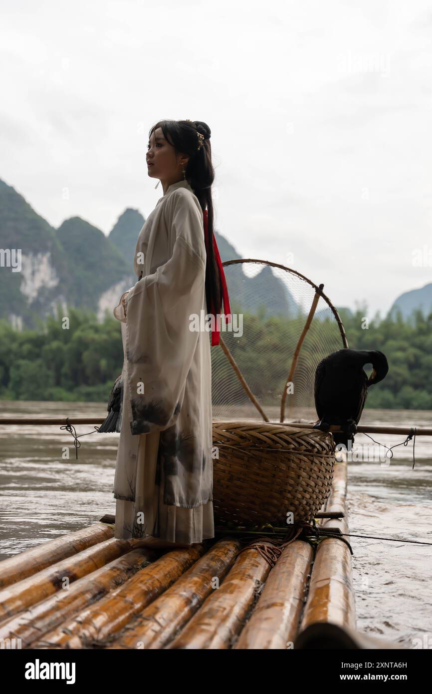 Chinesisches Hanfu-Mädchen, das ihre Haare repariert, während es auf einem Bambusfloß am Fluss Li, Xingping, steht Stockfoto