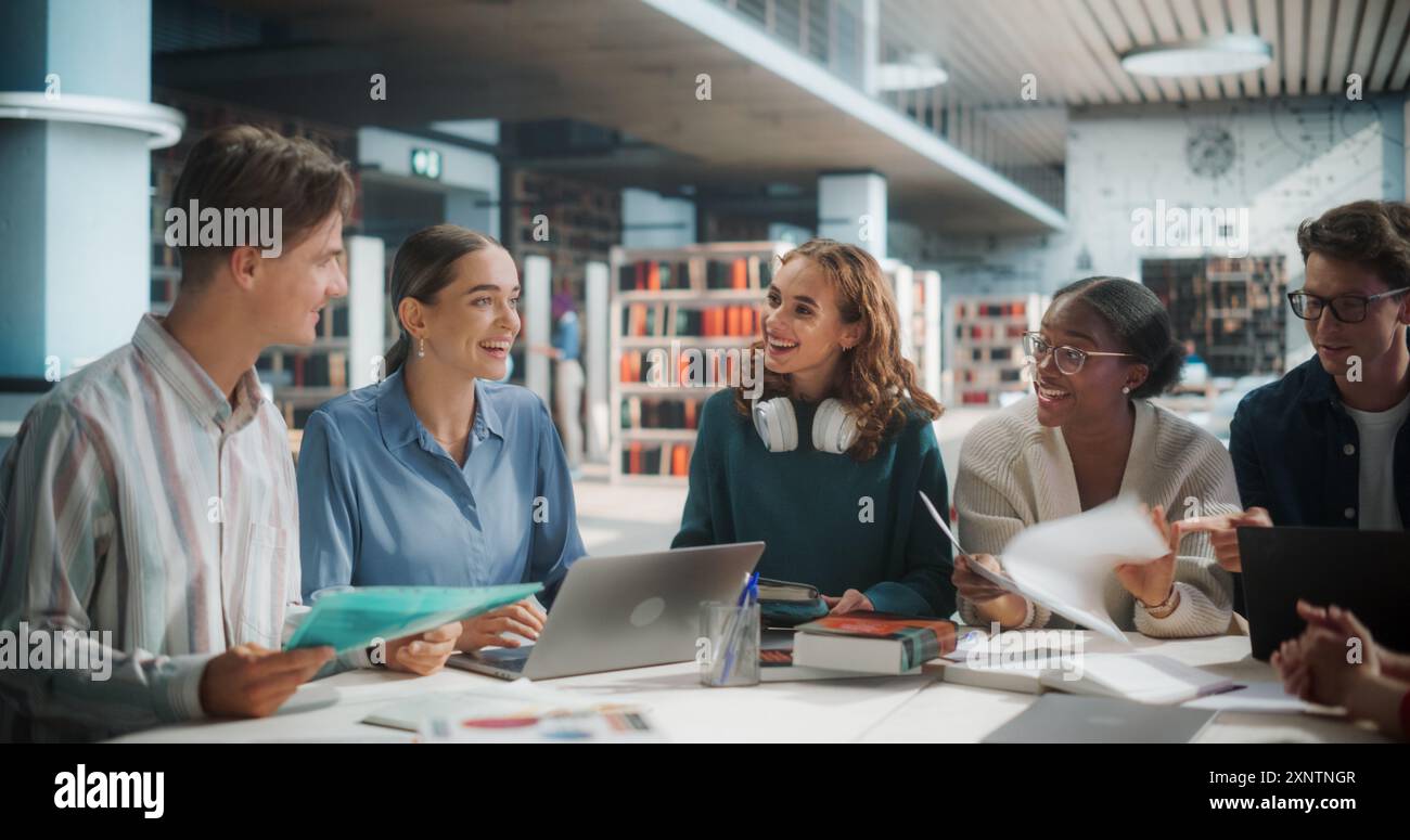 Verschiedene Gruppe von Studenten, die an einem Projekt in einer modernen Bibliothek zusammenarbeiten. Junge Erwachsene, die sich mit Diskussionen beschäftigen, Laptop und Dokumente verwenden, lächeln und Ideen in einer Bildungsumgebung austauschen Stockfoto