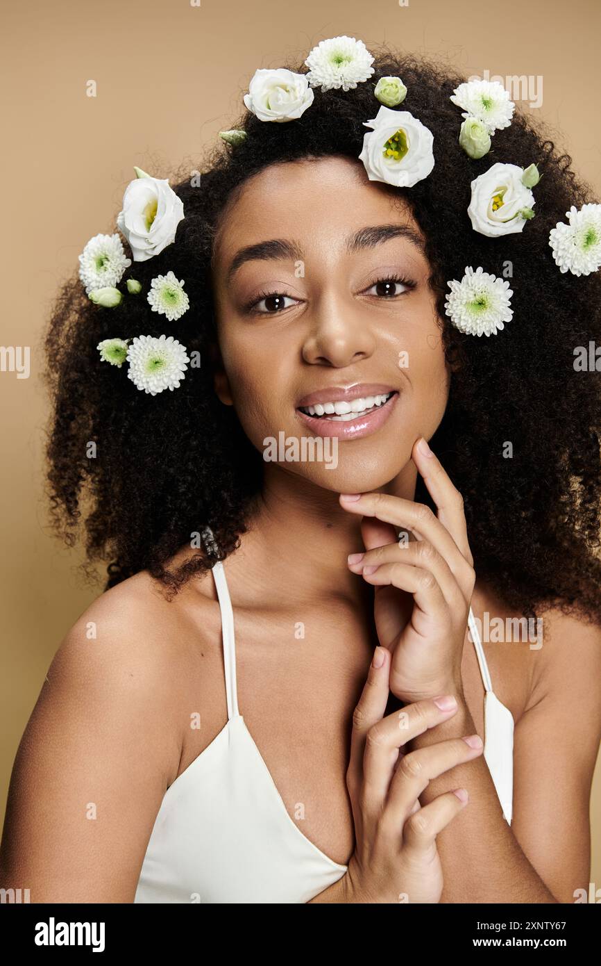 Eine schöne afroamerikanische Frau mit natürlichem Make-up und Blumen im Haar, die sanft lächelt, vor einem beigen Hintergrund. Stockfoto