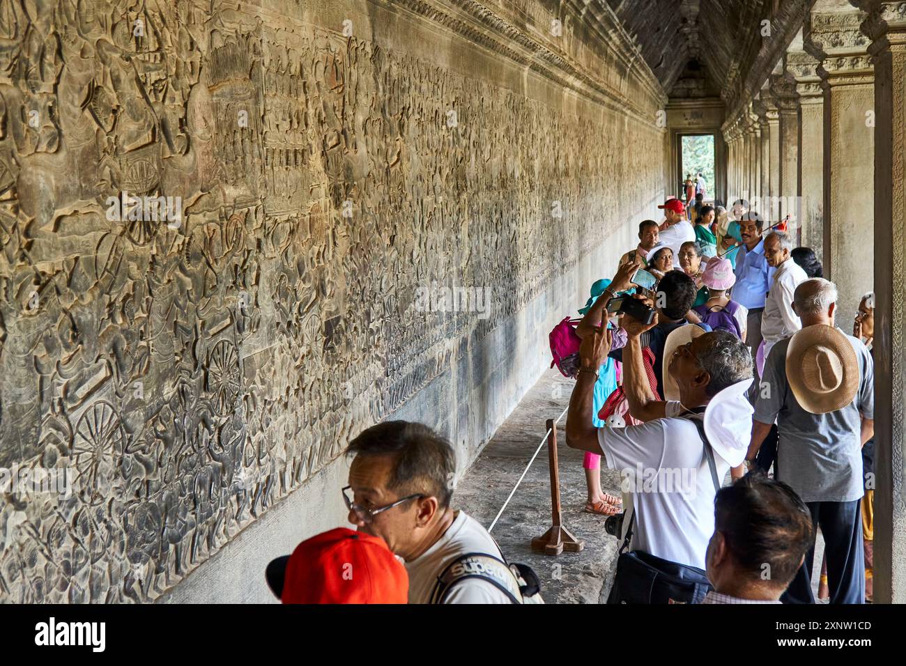 Eine Gruppe von Touristen erkundet und fotografiert die detaillierten Steinschnitzereien an den Wänden des Tempels Angkor Wat in Kambodscha. Stockfoto