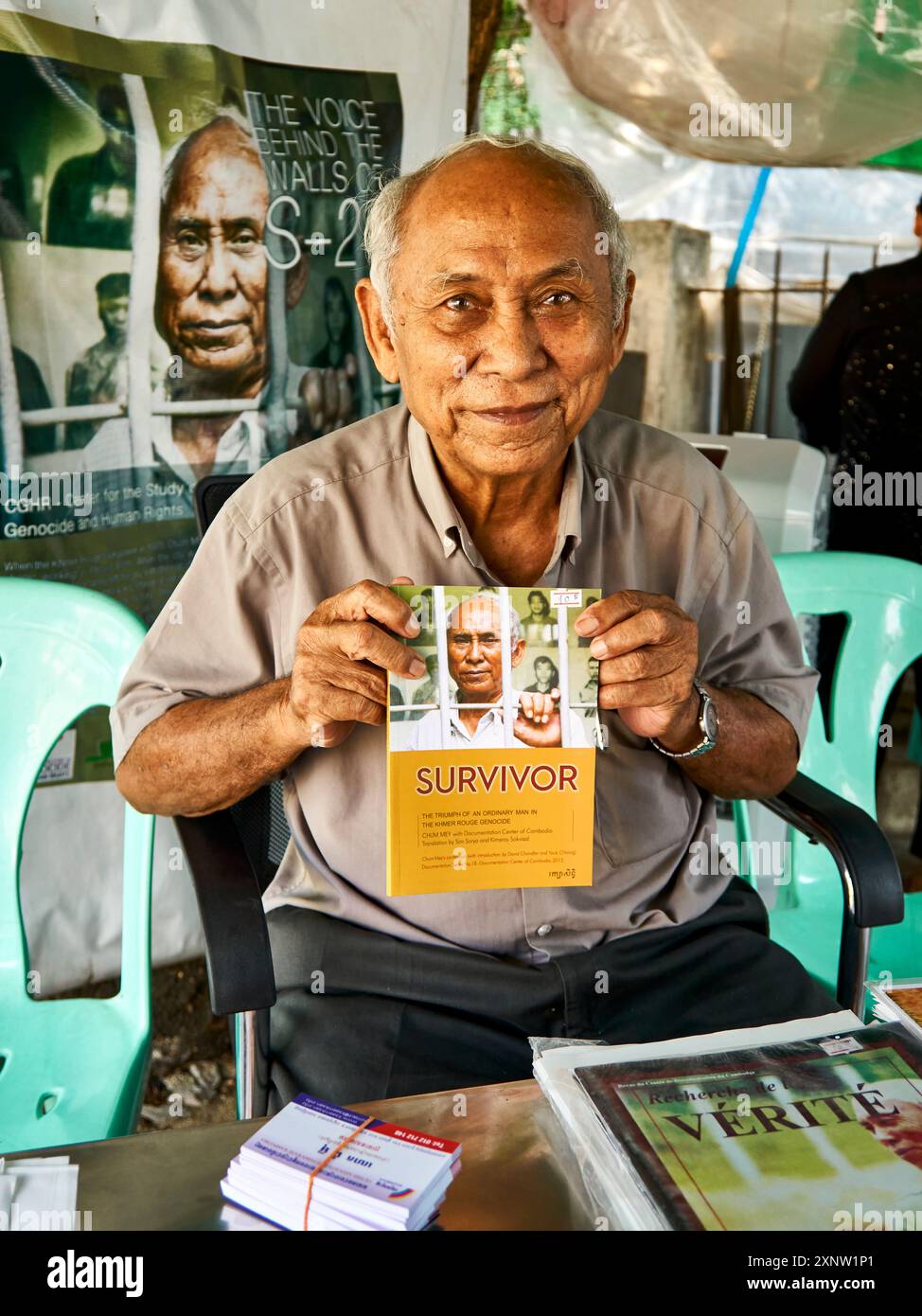 Ein älterer Mann hält stolz ein Buch mit dem Titel "Überlebender" in Phnom Penh, Kambodscha. Er erscheint inhaltlich und nachdenklich an einem Buchstand. Stockfoto