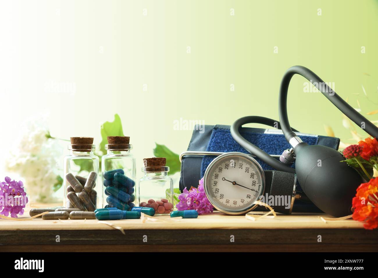 Konzept pflanzlicher Naturheilmittel zur Behandlung von Blutdruckproblemen mit Glasflaschen, Blutdruckmessgerät und Holzblüten Stockfoto
